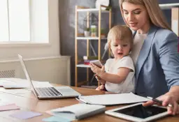 Kobieta z dzieckiem przy biurku z laptopem i tabletami. Czy na urlopie macierzyńskim można pracować na umowę zlecenie?