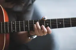 Dłoń z czarnym lakierem na paznokciach gra akord na gitarze. Najcieńsza struna to kwinta, tworząc melodię.