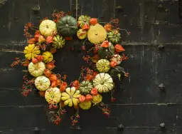 Jesienne ozdoby DIY: wieniec z dyni, miechunki i gałązek z czerwonymi owocami na ciemnym, drewnianym tle.
