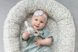 Niemowlę w kokonie z motywem roślinnym, trzymające zabawkę-króliczka.