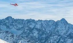 Czerwony helikopter ratunkowy lata nad ośnieżonymi Tatrami.