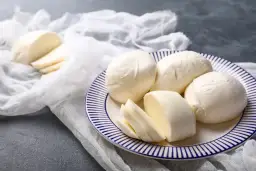 Świeża mozzarella na talerzu, pokrojona i w całości. Czy mozzarella podnosi cukier? Ten ser jest niskowęglowodanowy.