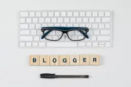 Wpis na bloga matura angielski: klawiatura, okulary i kostki z napisem BLOGGER.