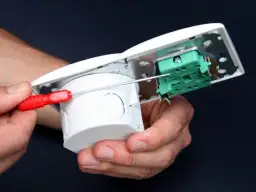 Ręce montują puszkę instalacyjną, podłączając zasilanie z włącznika światła.