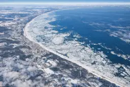 Zimowy krajobraz nad Bałtykiem, gdzie woda częściowo zamarzła, a na brzegu widać zaśnieżone miasteczko. Czy Bałtyk może zamarznąć? Tak, w mroźne zimy.