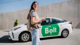 Kobieta z telefonem stoi obok białego samochodu Bolt z zielonym logo.