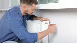 Mężczyzna używa śrubokręta, by prawidłowo odpowietrzyć grzejnik, pozbywając się powietrza z instalacji.