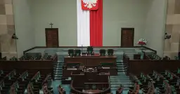 Pusta sala sejmowa z rzędami zielonych foteli i mównicą. Biało-czerwona flaga i godło Polski. Zastanawiasz się, ile jest posłów w sejmie?