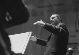 Igor Strawiński dyryguje, interpretując swoje kompozycje. Widać nuty i jego gestykulację.