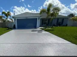 Nowy podjazd z jasnoszarym żwirem, idealnie pasujący do domu z niebieską bramą garażową.