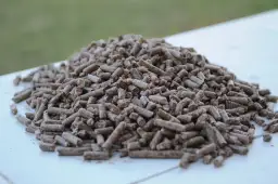 Góra drobnych, brązowych pelletów, idealnych jako dodatek do pelletu, leży na białej powierzchni.