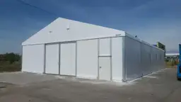 Duży biały namiot magazynowy z drzwiami i bramą. Czy postawienie namiotu magazynowego wymaga pozwolenia na budowę?