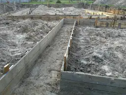 Wykonano wykopy pod fundamenty. Drewniane szalunki wyznaczają kształt przyszłego budynku na piaszczystym terenie budowy.