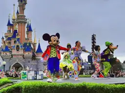 Myszka Miki i przyjaciele tańczą na scenie przed zamkiem w Disneylandzie w Paryżu.