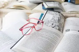 Różowe okulary leżą na otwartych książkach. Idealne do czytania po francusku, gdy tekst jest trudny.