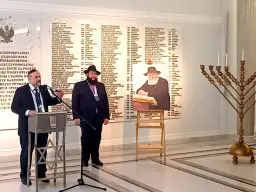 Dwóch mężczyzn w strojach religijnych, tablica z nazwiskami i menora.