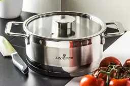 Stalowy garnek z logo Zwinger, idealny do przygotowania sosu pomidorowego. Obok nóż i świeże pomidory.