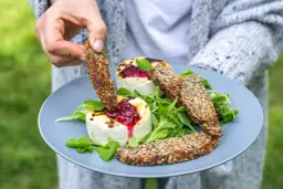 Ręka zanurza chrupki chleb pełen ziaren w grillowanym serze z konfiturą. Czy chleb tuczy? Ten z pewnością jest zdrowy!