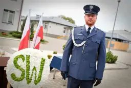 Funkcjonariusz Służby Więziennej w mundurze, obok wieńca z napisem SW i flag Polski.