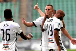 Piłkarze Legii Warszawa w białych strojach, jeden z nich pokazuje kciuk w górę.