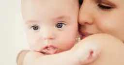 Zbliżenie na twarz niemowlaka trzymanego przez matkę, z widocznymi oczami dziecka i ustami matki.