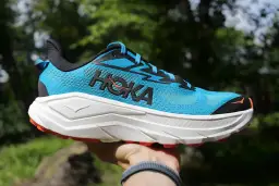 Niebieski but Hoka Challenger 8 z białym, grubym podeszwą i pomarańczowymi akcentami, gotowy na przygodę.