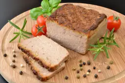 Upieczony pasztet na desce z pomidorkami, rozmarynem i pieprzem.
