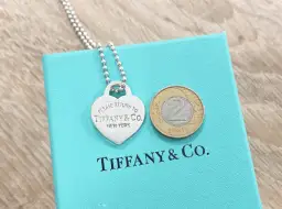 Srebrne serce z napisem "Please Return to Tiffany & Co. New York" na turkusowym pudełku Tiffany & Co. z monetą 2 złote.