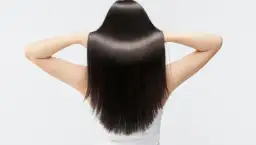 Kobieta z długimi, lśniącymi, ciemnymi włosami, odsłoniętymi ramionami.