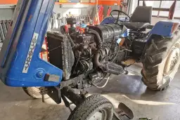 Niebieski Ursus z otwartą maską, widoczny silnik i koła.