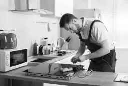 Instalator pracuje nad podłączeniem płyty indukcyjnej, przygotowując się do montażu piekarnika.