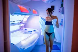 Kobieta w bikini wychodzi z solarium, niosąc ręcznik. Uważaj na oparzenie po solarium, bo może być bolesne.