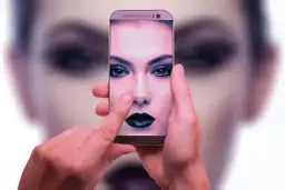 Dłonie trzymają smartfon, na ekranie którego widać twarz kobiety z mocnym makijażem. To przykład zaawansowanej fotografia obliczeniowa.