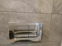 Chromowany przycisk spłuczki podtynkowej na szarej płytce. Dowiedz się, jak zdemontować przycisk spłuczki podtynkowej.