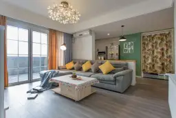 Nowoczesne oświetlenie pokoju tworzy przytulną atmosferę. W centralnym punkcie wisi designerska lampa, a obok niej stojąca lampa rzuca ciepłe światło na szarą sofę.