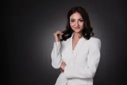 Elegancka kobieta w białej marynarce, uśmiecha się pewnie. To profesjonalne zdjecie biznesowe.