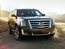 Ciemny Cadillac Escalade na tle gór i suchej trawy.