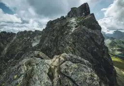 Kamienista trasa na Kozi Wierch, z łańcuchami ułatwiającymi wspinaczkę. Dramatyczne chmury nad skalistymi szczytami Tatr.