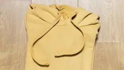 Żółta bluza z kapturem złożona na drewnianym tle.