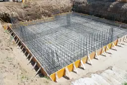 Zbrojenie fundamentów domu w wykopie, otoczone szalunkiem.