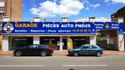 Garage avec enseigne bleue et jaune, deux voitures garées devant, sous un ciel bleu avec des nuages.