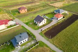 Widok z lotu ptaka na kilka domów jednorodzinnych na tle pól i zieleni.
