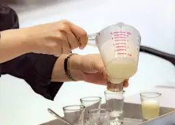 Ręce przelewają płyn z miarki do kieliszków.