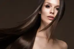 Portret kobiety z długimi, brązowymi włosami, część twarzy i ramion.