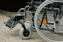 Zbliżenie na wózek inwalidzki z widocznymi kołami i podnóżkiem.