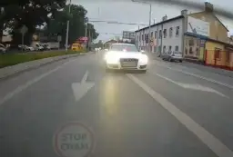 Białe Audi S7 z włączonymi światłami i sygnałem świetlnym jedzie ulicą. Kierowca tego auta prawdopodobnie spieszy się na interwencję.