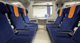 Wnętrze wagonu TLK z niebieskimi siedzeniami i pomarańczowymi zagłówkami. Obok siedzeń widać zielone lampki, co sugeruje, że czy w TLK są kontakty.