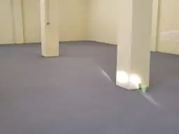 Nowa, szara posadzka betonowa w domu, z jasnymi filarami i żółtymi ścianami.