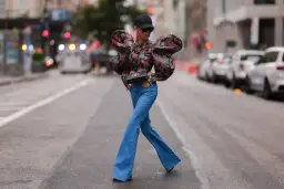 Modna kobieta w jeansach dzwonach i kwiecistej bluzce z bufiastymi rękawami, prezentująca stylowe jeansy dzwony stylizacje na ulicy.