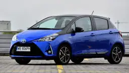 Niebieska Toyota Yaris Hybrid, z czarnym dachem, zaparkowana na zewnątrz. Ile koni ma Toyota Yaris? Ten model ma 100 KM.